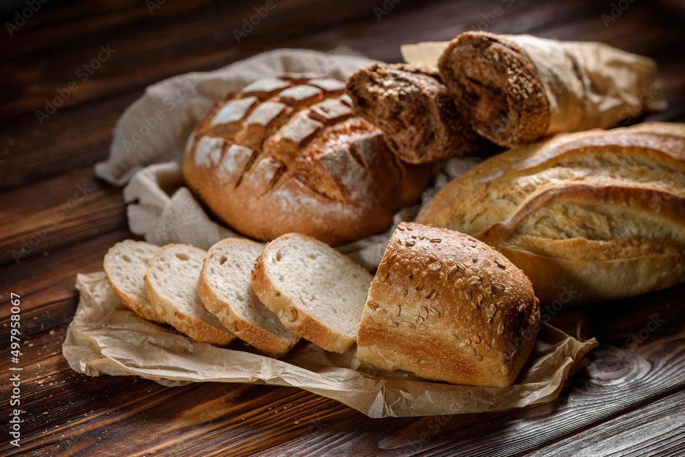 Bakery products on the kitchen rustic table. Various types of fresh fragrant crispy freshly baked bread on a wooden background. Appetizing bun and baguettes close-up. Healthy food and bakery concept.