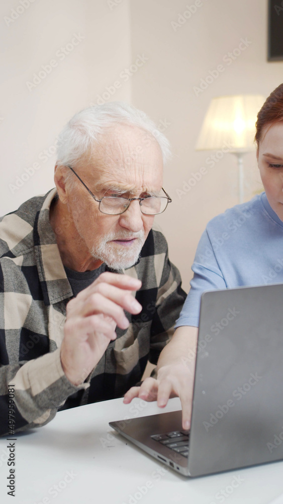 A nurse brings a pensioner in a wheelchair to the workplace. She opens the laptop, gives glasses and helps him A nurse brings a pensioner in a wheelchair to the workplace. She opens the laptop, gives glasses and helps him