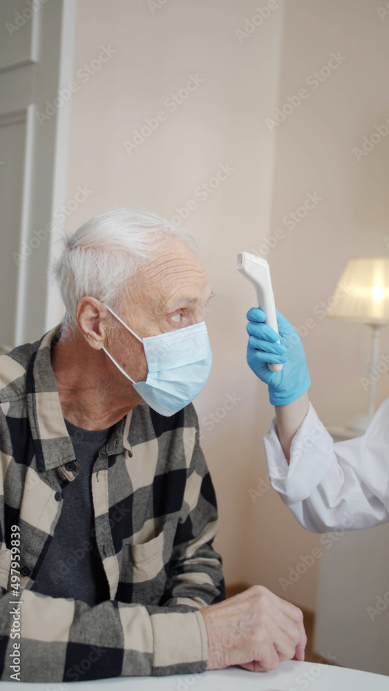 An orderly examines an elderly patient, measures the temperature and fills out a medical record