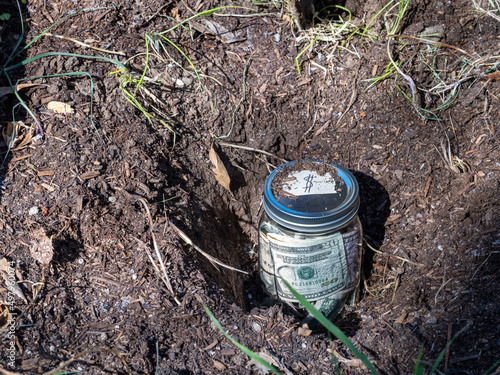 Burying a jar of money in the garden as savings, retirement or college fund concept. photo