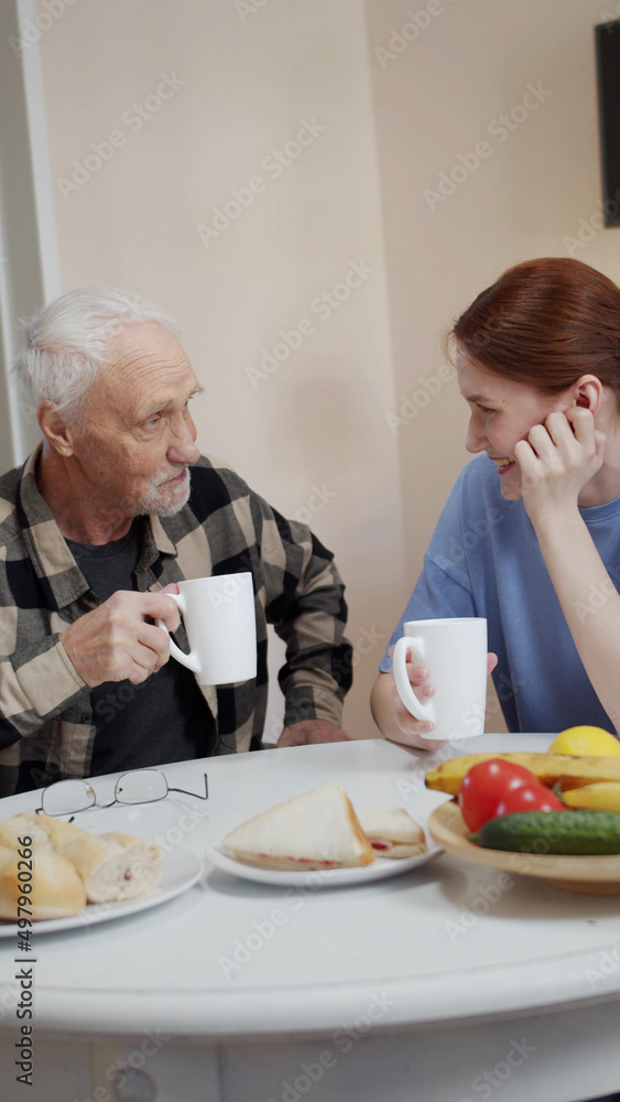 Family get togethers. Woman drinking tea with her elderly father and clinking glasses