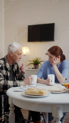 Grandfather in a wheelchair chatting with a young woman over a cup of coffee