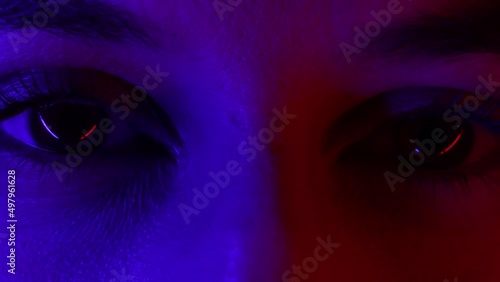 Neon colored, ultraviolet light woman's eye macro shot. Glowing disco night, red and blue lights and close up shot of beautiful woman eye.
