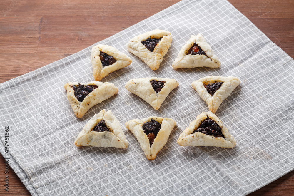 Gomentashash with poppy seeds and prunes freshly baked for the holiday of Purim on a gray checkered towel. Gomentashash with poppy seeds and prunes freshly baked for the holiday of Purim on a gray checkered towel.