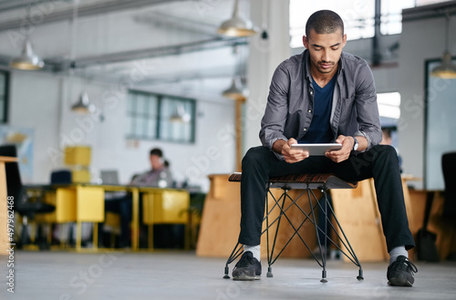 Hes a tech savvy young designer. Shot of a young man using a digital tablet while sitting in a modern office.