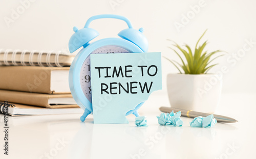 Flower in a pot, calculator, white alarm clock, multi-colored pieces of paper and a white notebook with the text TIME TO RENEW on the desktop