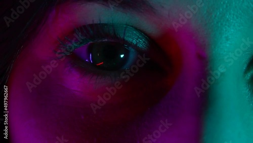 Neon colored, ultraviolet light woman's eye macro shot. Glowing disco night, red and blue lights and close up shot of beautiful woman eye.