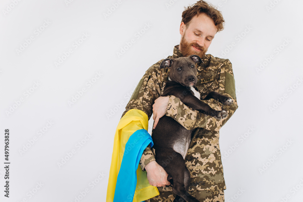 Ukrainian soldier in military uniform with a yellow and blue flag holds a dog in his arms on a white background