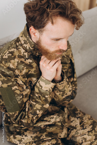 Portrait of emotional young bearded Ukrainian patriot soldier in military uniform sitting on the office sofa