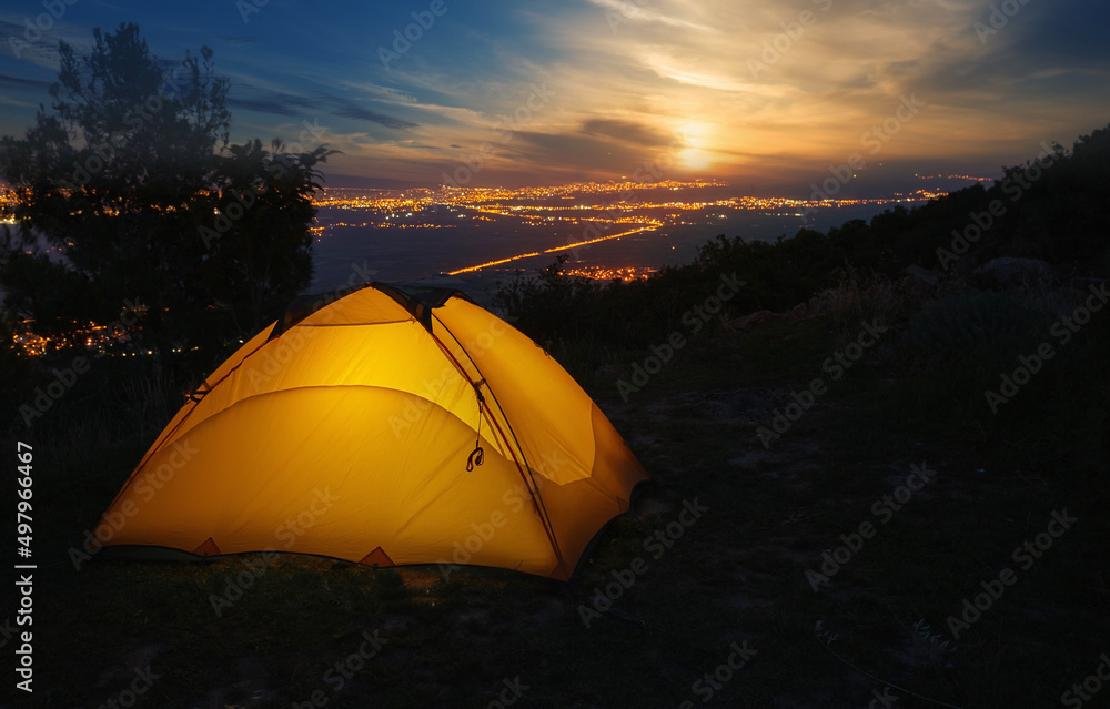 Orange tourist tent against backdrop of city lights at sunset