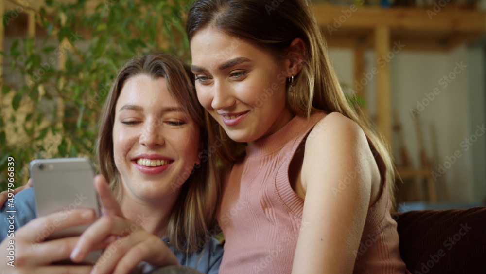 Two beautiful women are sitting together on the sofa and choosing the best one of the photos they made Two beautiful women are sitting together on the sofa and choosing the best one of the photos they made