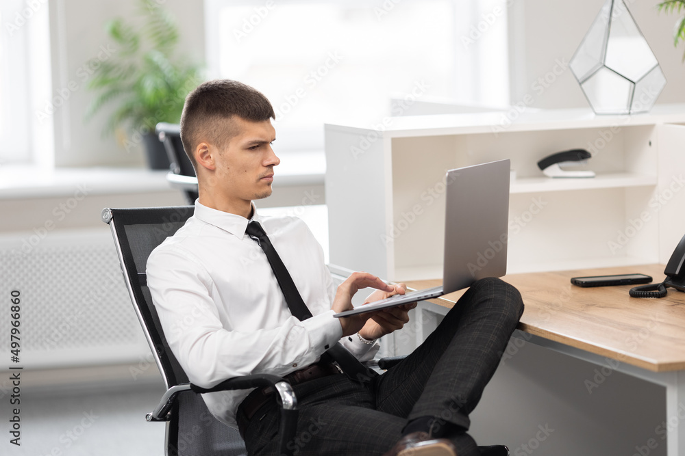 attractive man in the office holding a laptop on his lap attractive man in the office holding a laptop on his lap