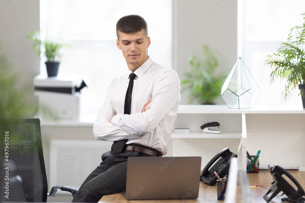attractive man in the office sits at the desk and looks at the laptop attractive man in the office sits at the desk and looks at the laptop