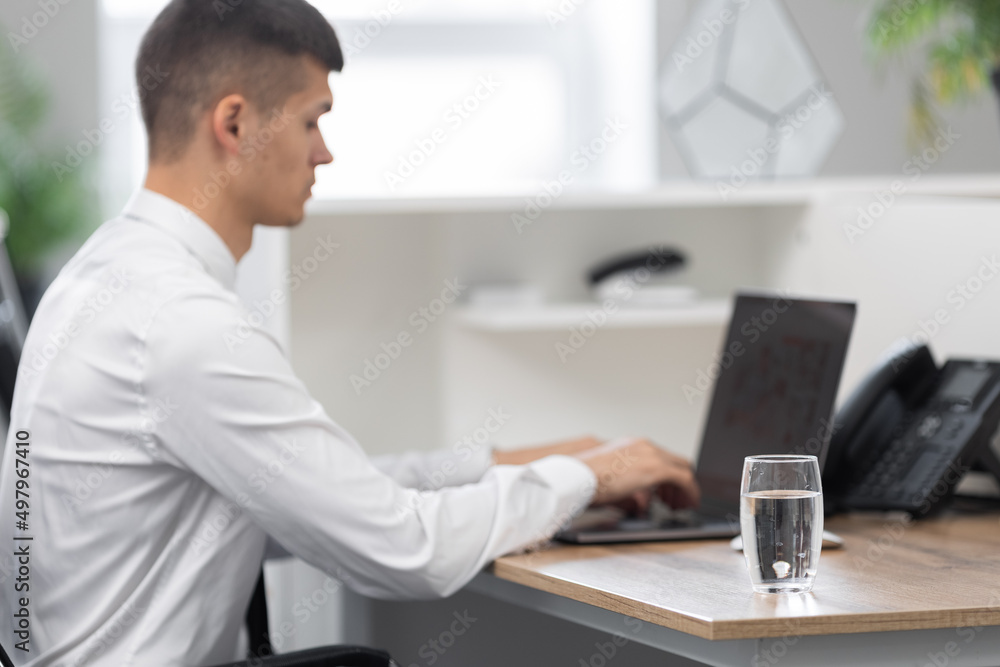 attractive young man in the office at work, next to him on the table in a glass of clean water