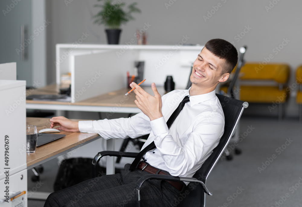 Successful happy business man sitting at a desk in the office, and uses a laptop.