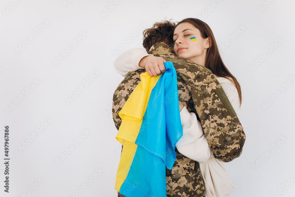 Fototapeta premium A Ukrainian girl hugs and holds a yellow and blue flag of a military man in uniform and says goodbye to him.