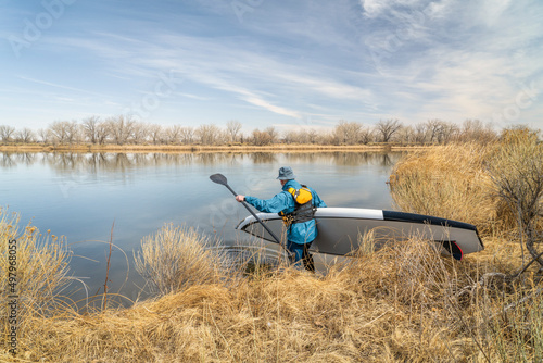 male stand up paddler is launching his paddleboard on a calm lake in early spring scenery in Colorado