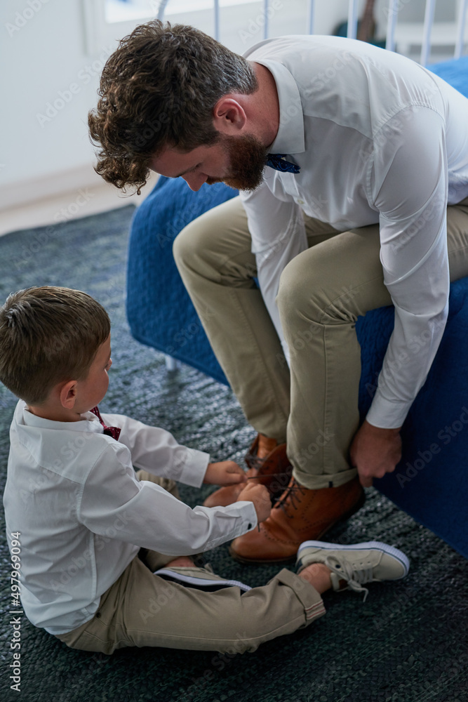 Fototapeta premium Helping Daddy tie his shoelaces. Cropped shot of an adorable little boy tying his fathers shoelaces at home.