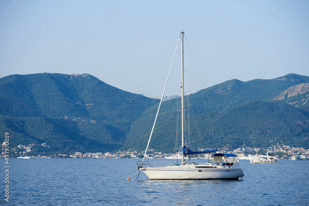White yacht with lowered sails in the Adriatic sea against the backdrop of mountains White yacht with lowered sails in the Adriatic sea against the backdrop of mountains