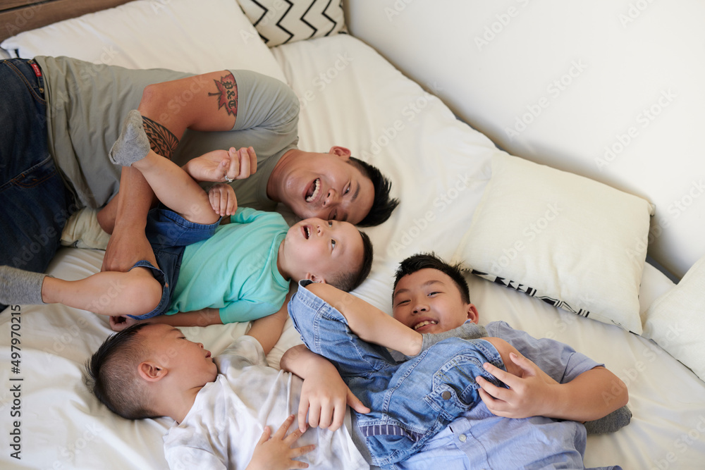 Joyful father and his three sons relaxing on bed when spending weekend together at home Joyful father and his three sons relaxing on bed when spending weekend together at home