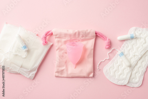 Top view photo of pink period pad bag menstrual cup sanitary napkins and tampons on isolated pastel pink background. Uterus and ovaries concept photo