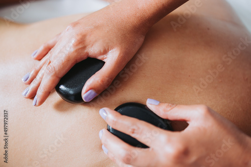 Therapist placing hot spa volcanic lava stone on a female patient's back. Energy stones.
