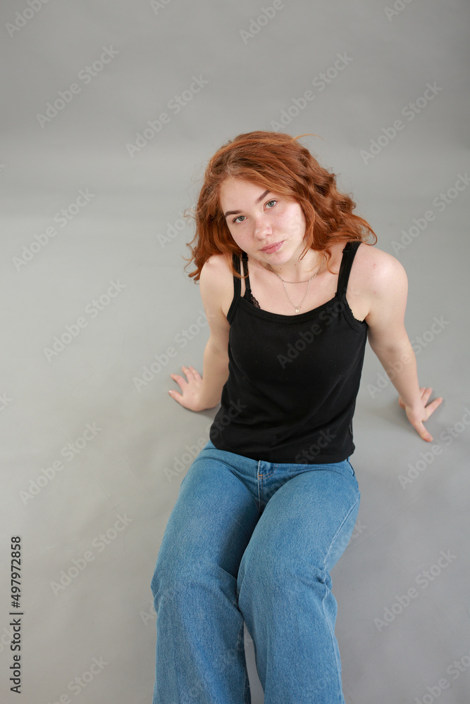 beautiful young girl model redhead. model in jeans and black top on a gray background. studio shooting. model with red hair and unusual appearance. beautiful young girl model redhead. model in jeans and black top on a gray background. studio shooting. model with red hair and unusual appearance.