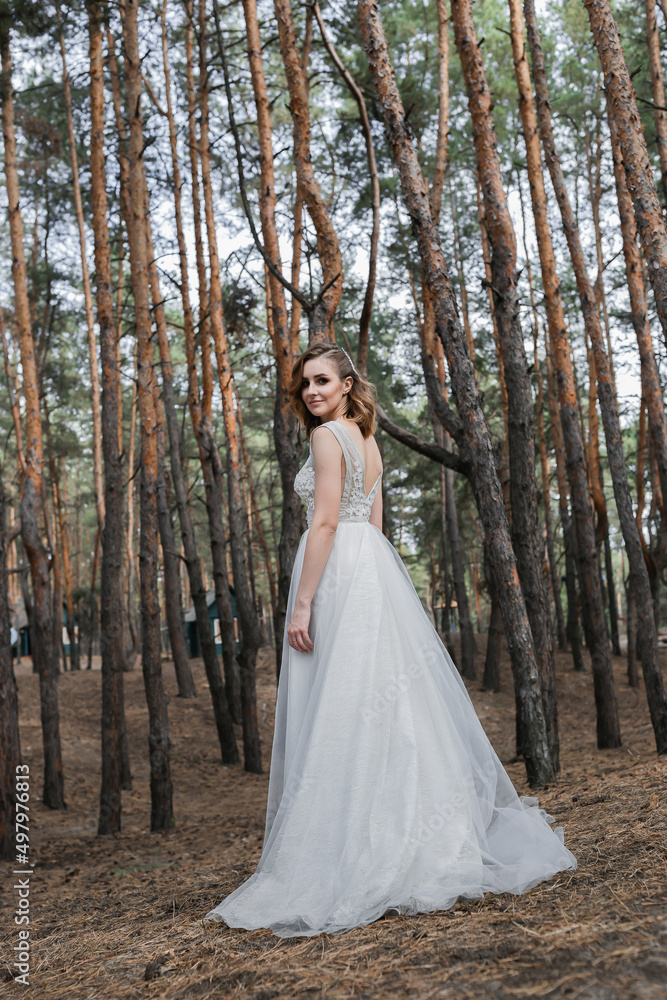 A beautiful, satisfied bride in a pine forest poses.