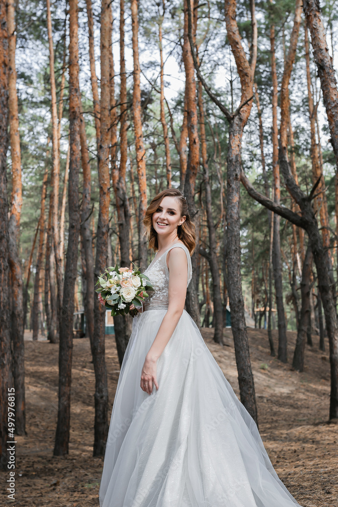 A beautiful, satisfied bride in a pine forest poses.
