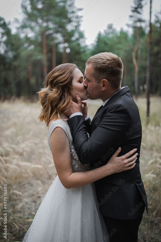 Wedding couple in the park. An elegant bride of European appearance and a groom in a black suit.