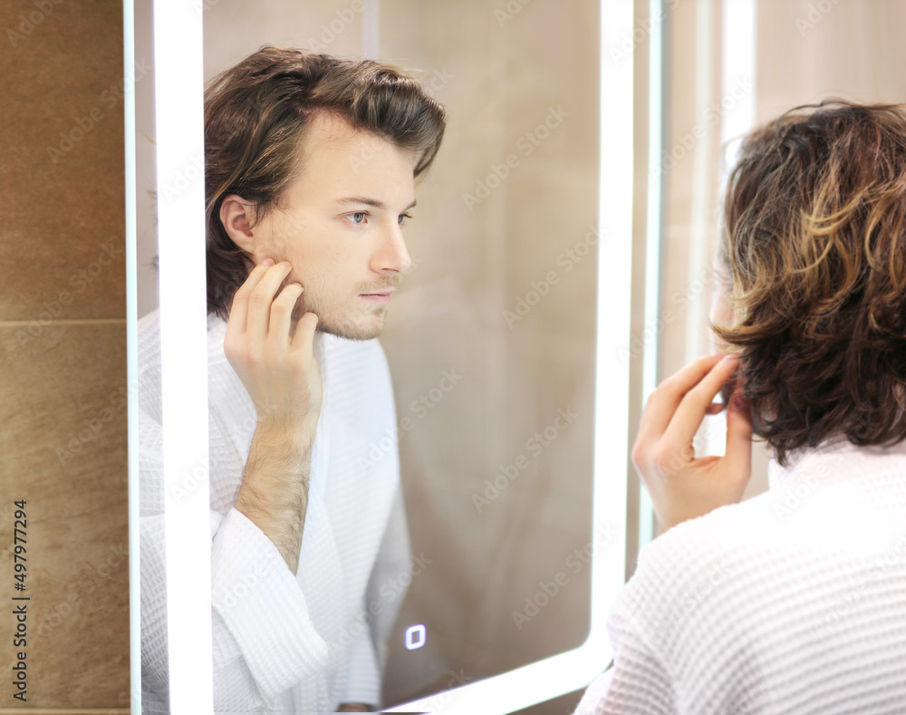 young man looking in the mirror,combing his hair,looking at problems on face. young man looking in the mirror,combing his hair,looking at problems on face.