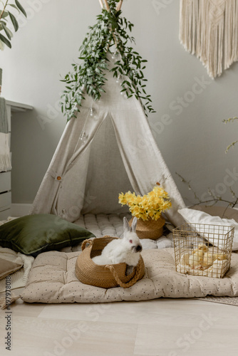 Spring children's photo zone with a wigwam. Children's interior. Rabbits, wigwam, spring branches, pillows, daffodils. Children's Easter photo zone with rabbits and chickens