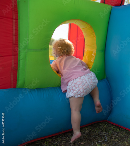 the kid climbs into the bouncy castle through a round window in the summer barefoot