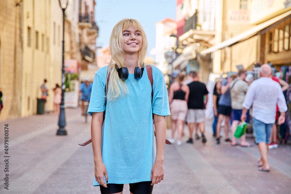 Young woman in headphones with backpack on street of tourist city