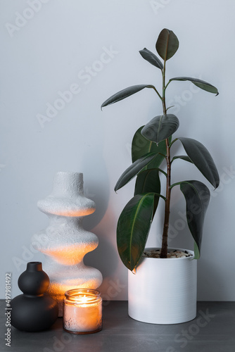 Home interior with decor elements. White and black decorative handmade vase and burning candle on a background of gray wall interior decoration.
