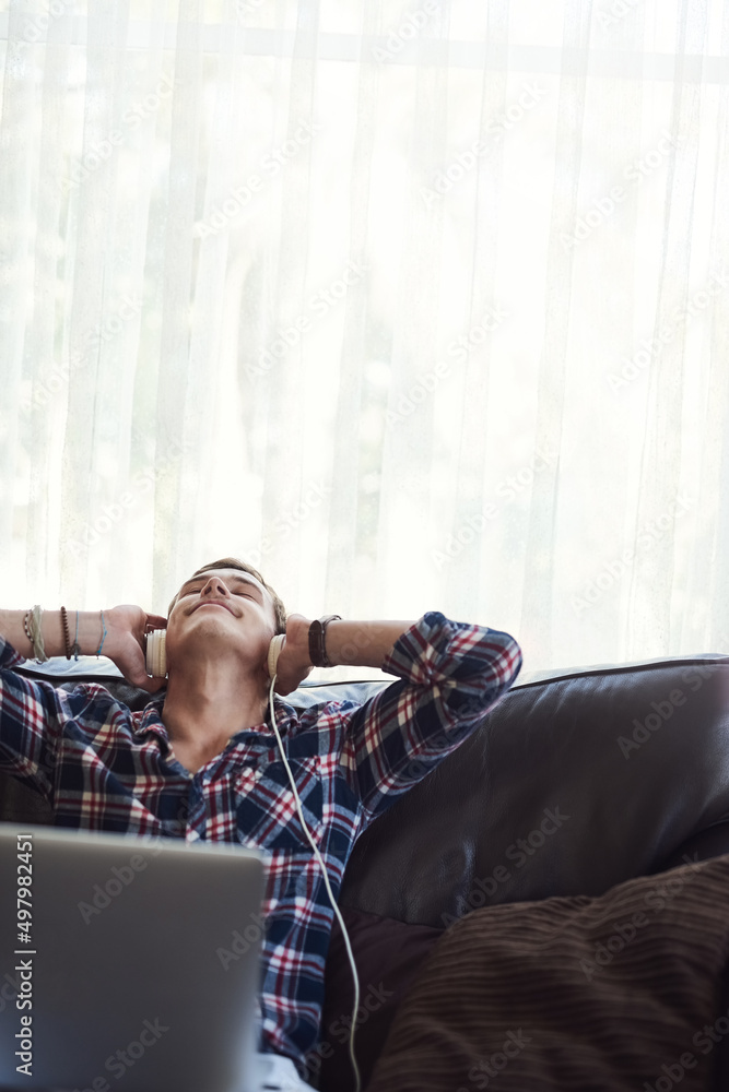 Getting lost in the music. Shot of a handsome young man using his laptop to listen to music while sitting on the sofa at home. Getting lost in the music. Shot of a handsome young man using his laptop to listen to music while sitting on the sofa at home.