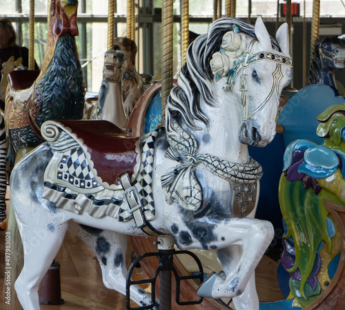 Fototapeta Naklejka Na Ścianę i Meble -  Carved white and black spotted horse with saddle and white roses on a carousel ride