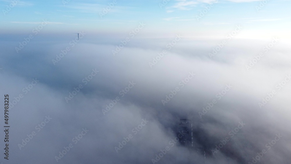 Aerial drone view flight over fog covering city. Scenic aerial view moving white foggy clouds and blue sky. Fog fast moving above rooftops of city houses. Sky landscape. Nature background. Environment Aerial drone view flight over fog covering city. Scenic aerial view moving white foggy clouds and blue sky. Fog fast moving above rooftops of city houses. Sky landscape. Nature background. Environment