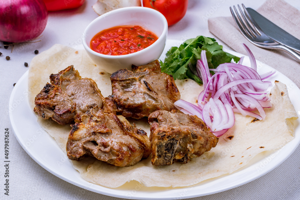 veal rib kebab on plate with red onion and tomato sause on white table