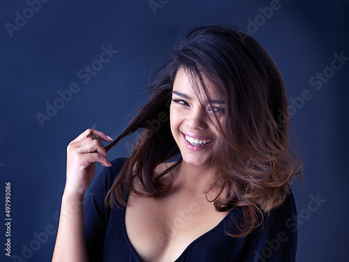 My hair never felt this good. Studio shot of a beautiful young woman playing with her hair against a blue background.
