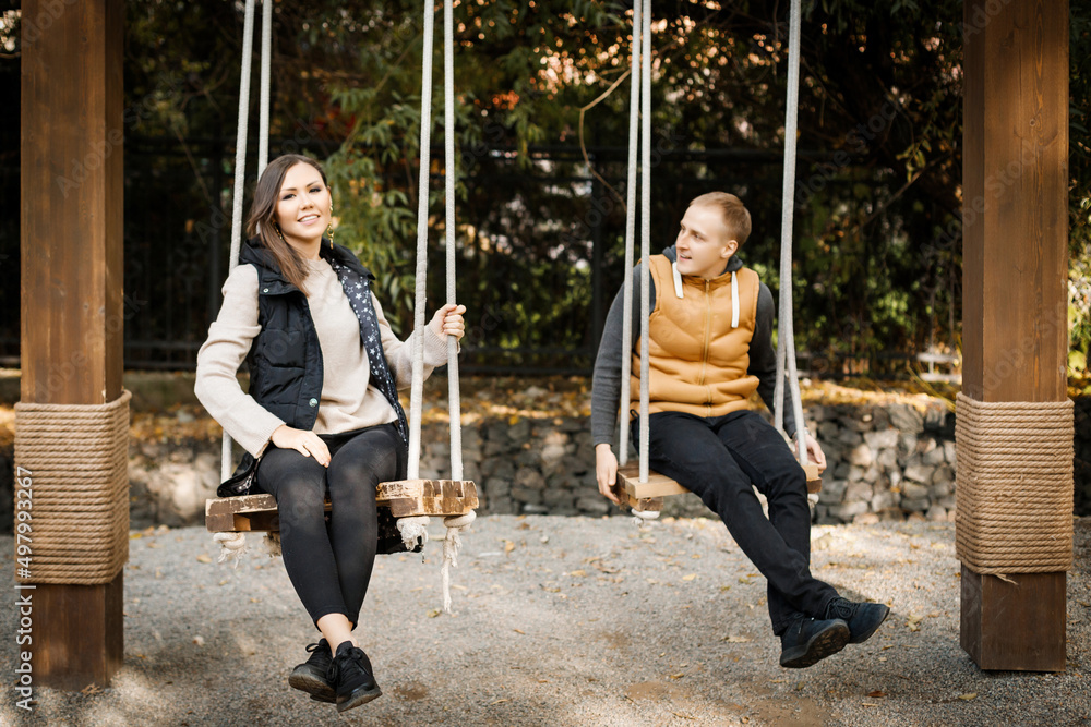 Obraz premium A young man with his lover are sitting on a swing in the forest among the trees.