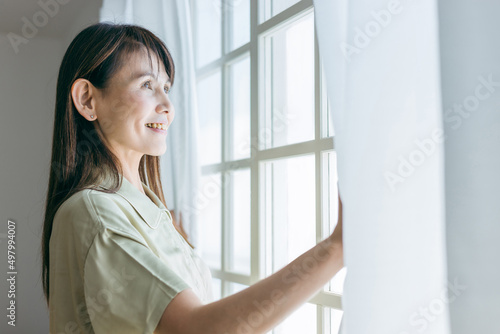 窓を開けるミドル世代の女性（パジャマ） 