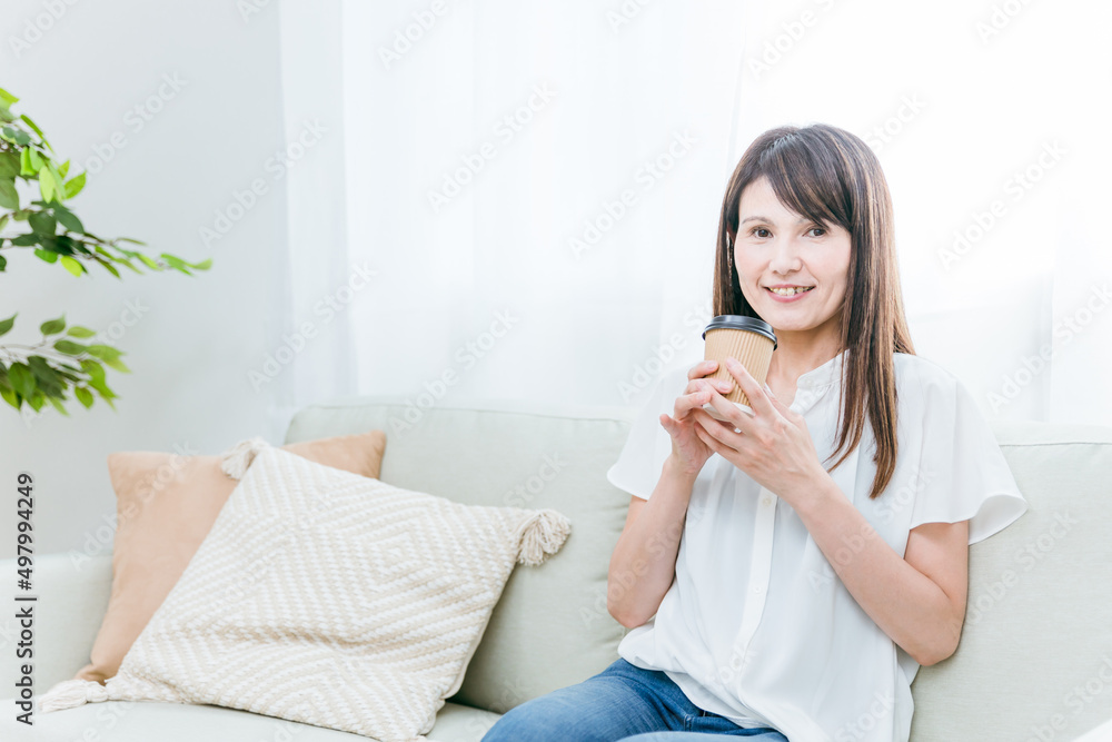 ソファでカップコーヒーを飲む中高年女性
ソファでカップコーヒーを飲む中高年女性