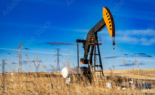 An oil pump jack working on an agriculture field with oil and gas equipment and distant power lines in Rocky View County Alberta Canada. photo