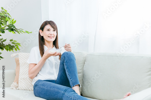 ソファでヨーグルトを食べる女性（笑顔） 