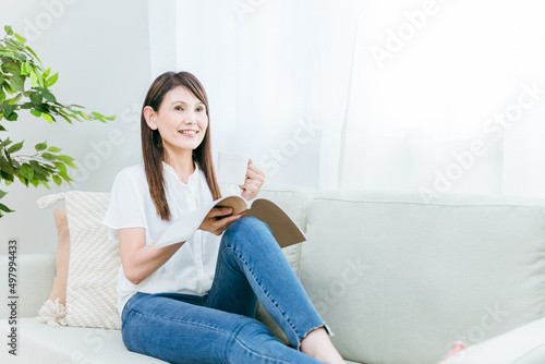ソファに座る中高年女性（飲み物、読書） 