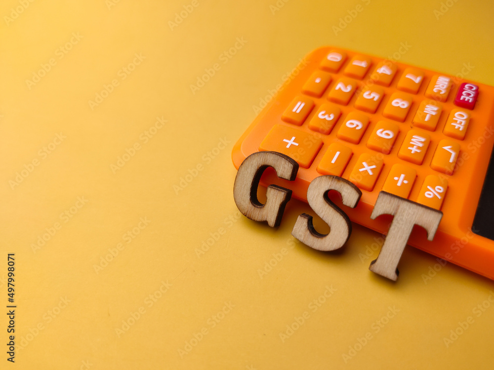 Calculator and wooden word with text GST on a yellow background. Calculator and wooden word with text GST on a yellow background.
