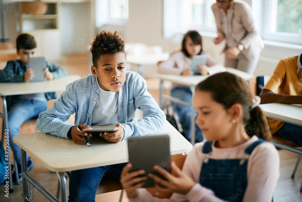Black elementary student and his classmate learn on digital tablets during computer class at school. Black elementary student and his classmate learn on digital tablets during computer class at school.