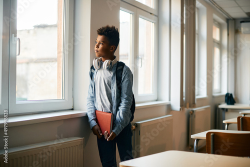 Pensive black schoolboy looks through the window in the classroom. photo