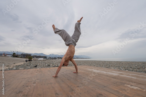 Shirtless caucasian man doing backflip on pebble beach. 